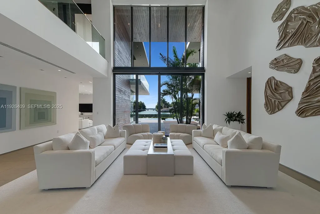 Waterfront exterior view of a tropical modern luxury residence at 6480 Allison Rd in Miami Beach, featuring floor-to-ceiling glass, resort-style pool, and bayfront access.