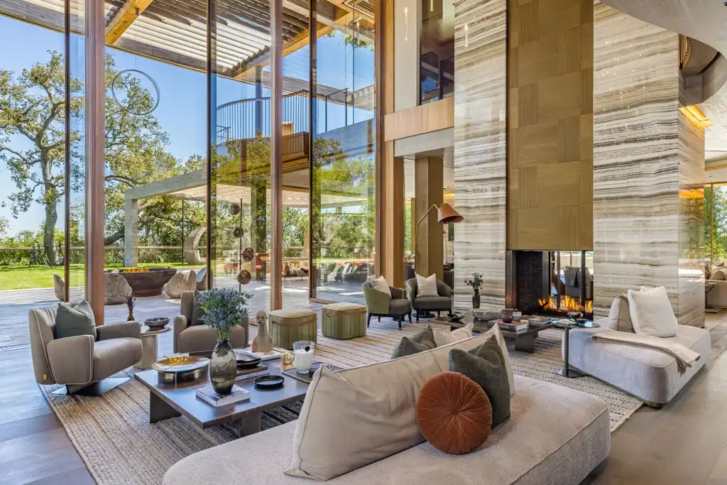 Most Expensive Homes in California 9 luxury living room with floor to ceiling glass walls and fireplace overlooking landscaped grounds