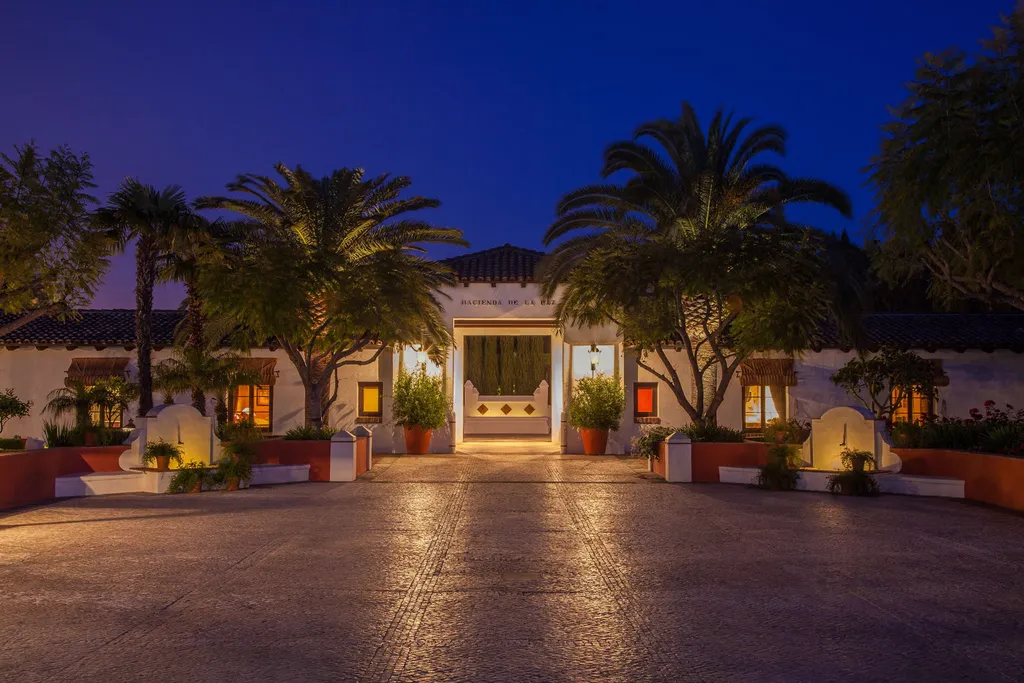 Hacienda de la Paz: One of the Largest Private Estates in California 2 Hacienda de la Paz entrance in Rolling Hills California at dusk with palm lined driveway and Spanish style architecture
