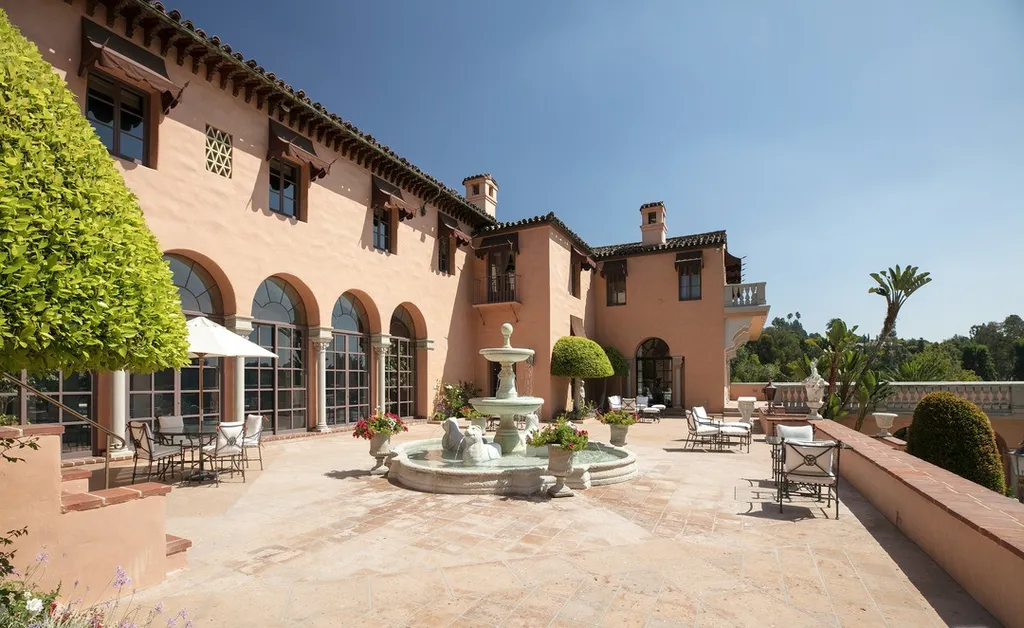 The Hearst Estate in Beverly Hills: A Historic Landmark Where Hollywood Legacy Meets Market Reality 13 The Hearst Estate in Beverly Hills featuring sunlit terrace with fountain, arched windows, and Mediterranean outdoor seating