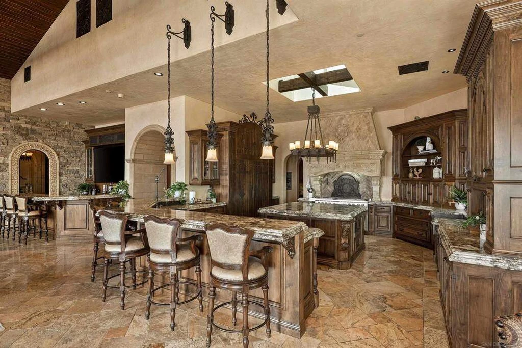 8619 Via Rancho Cielo – Island Kitchen 8619 Via Rancho Cielo, Rancho Santa Fe: a large stone island anchors the kitchen beneath exposed beams.